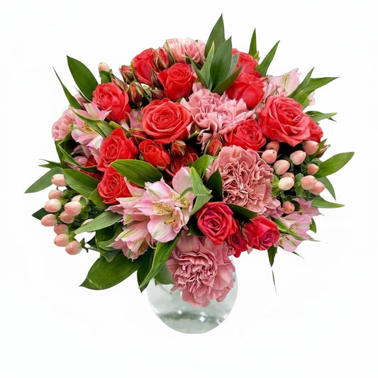 Flower Station bouquet with red roses, pink carnations, blush alstroemeria, and hypericum berries in a glass vase.